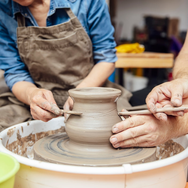 A close-up of a potter shaping a clay vase on a spinning pottery wheel, with hands covered in wet clay